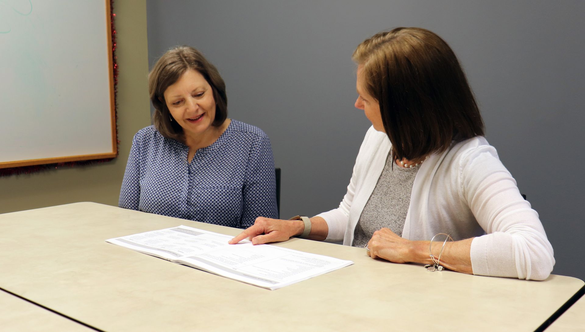 Two women are sitting at a table looking at a piece of paper. Two women are sitting at a table looking at a piece of paper.