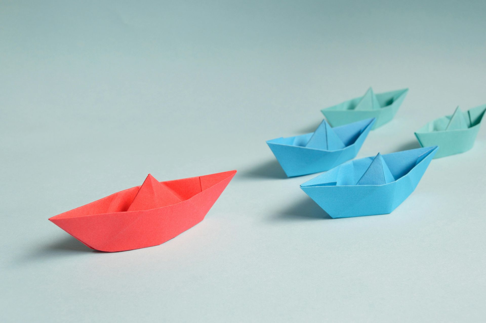 A red paper boat is leading a row of blue paper boats.