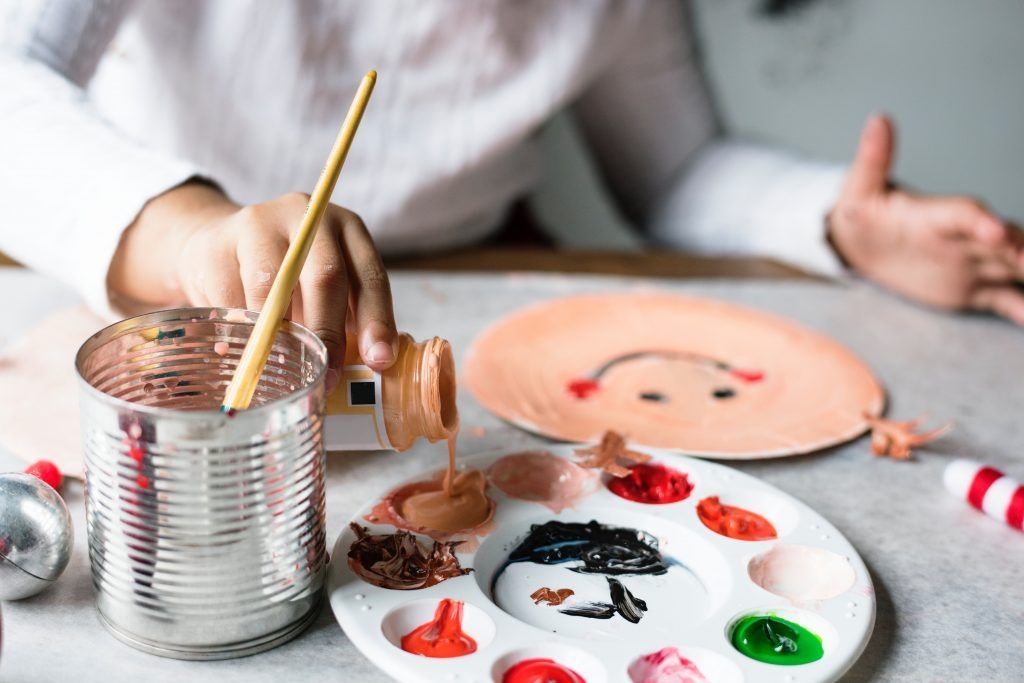A child is painting a paper plate with a brush.