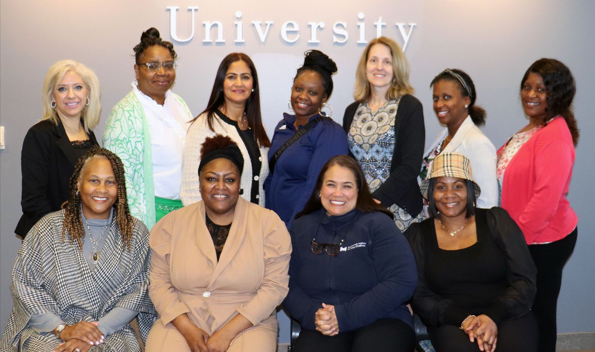 Woman in glasses smiles, arms crossed, in a brightly colored preschool classroom.
