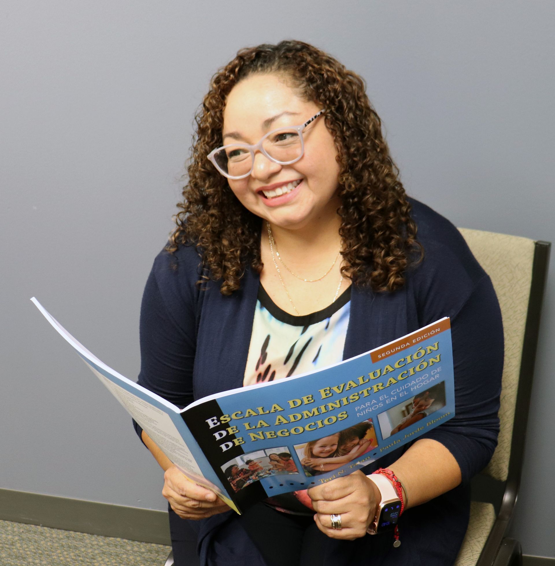 Woman with glasses, smiling, holding a Spanish book titled