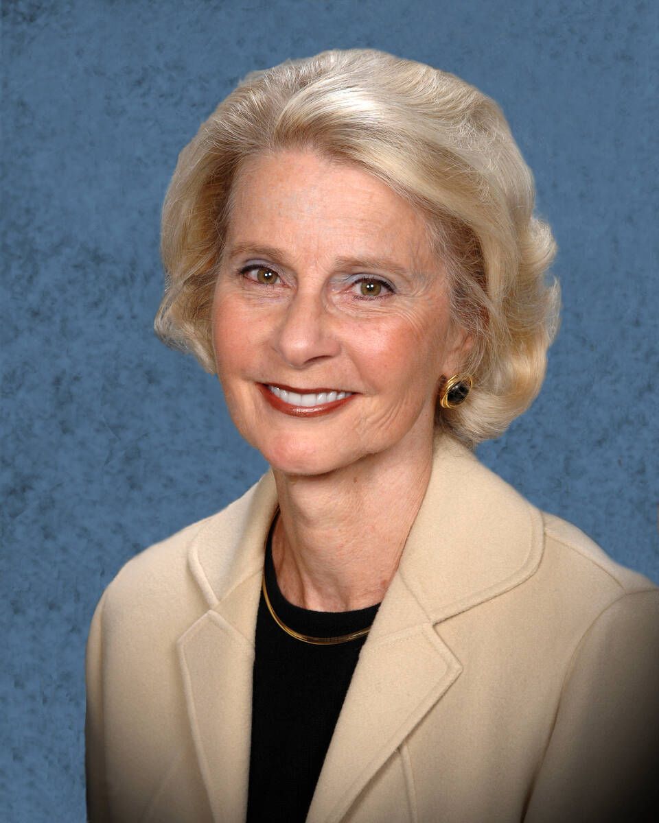 A woman in a tan jacket and black shirt smiles for the camera