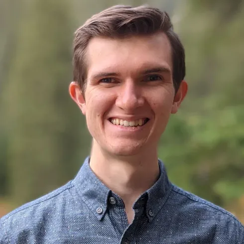 A young man in a blue shirt is smiling for the camera.