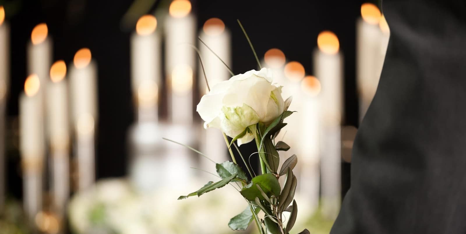 A person is holding a white rose in front of a row of lit candles.