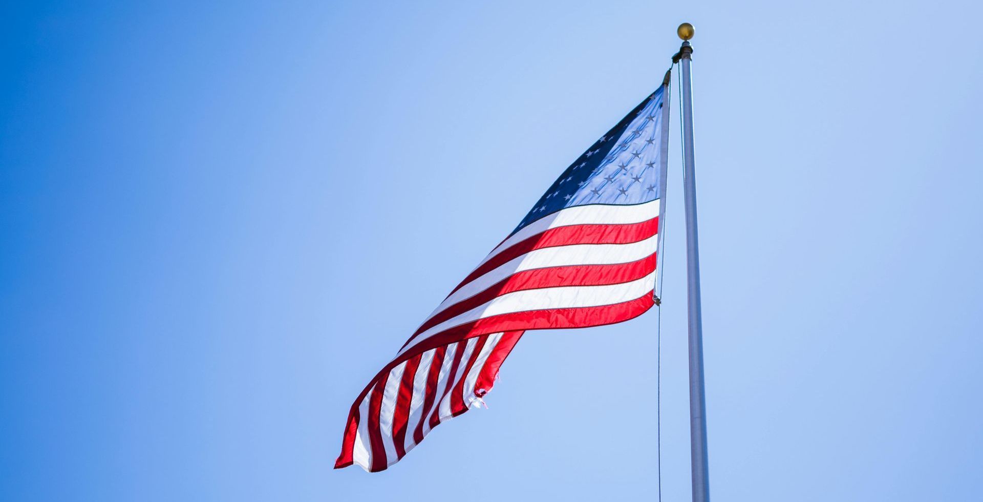 The american flag is waving in the wind against a blue sky.