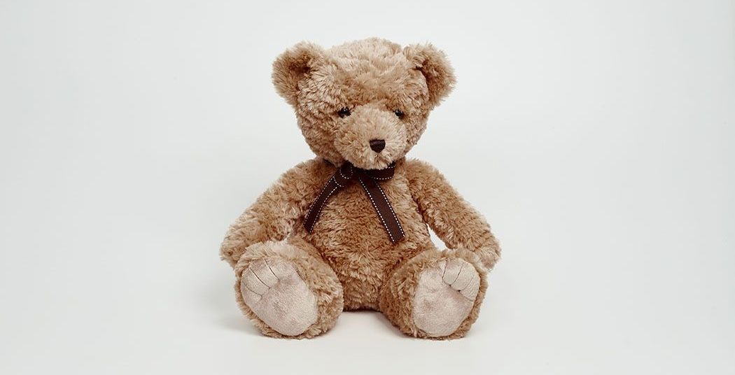 A brown teddy bear is sitting on a white surface.