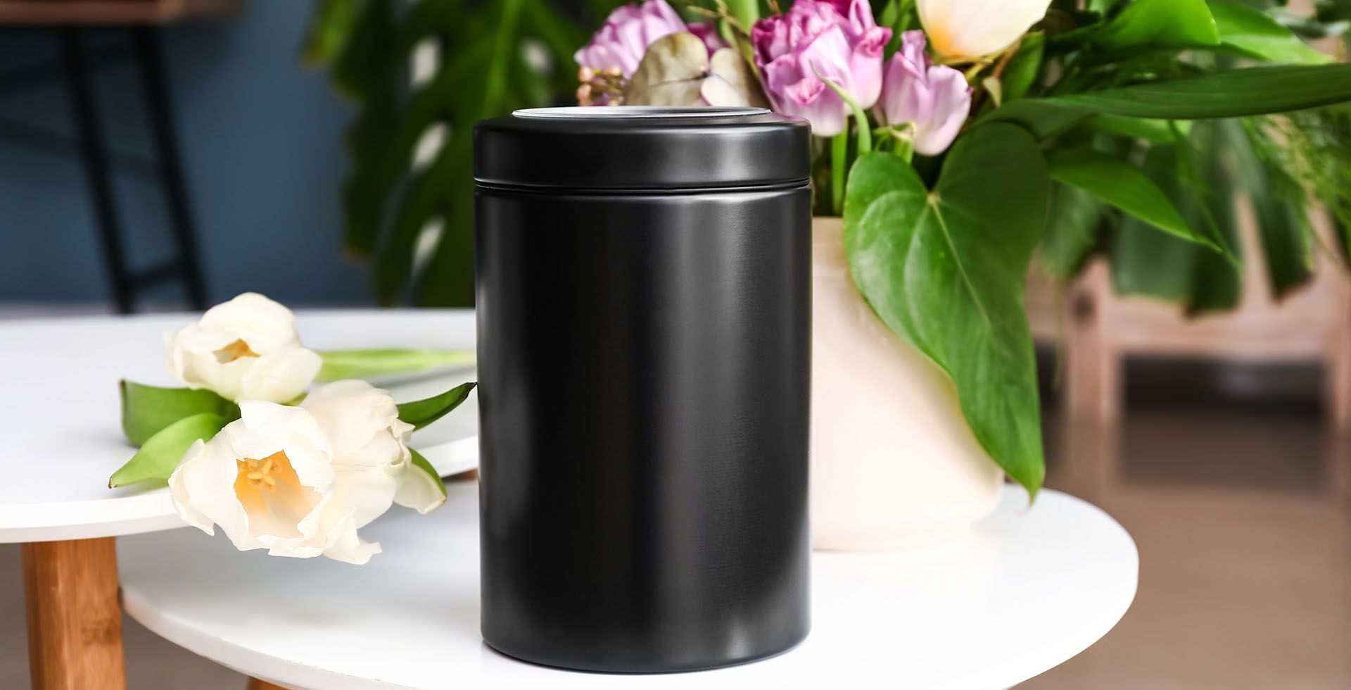 A black canister is sitting on a table next to a vase of flowers.