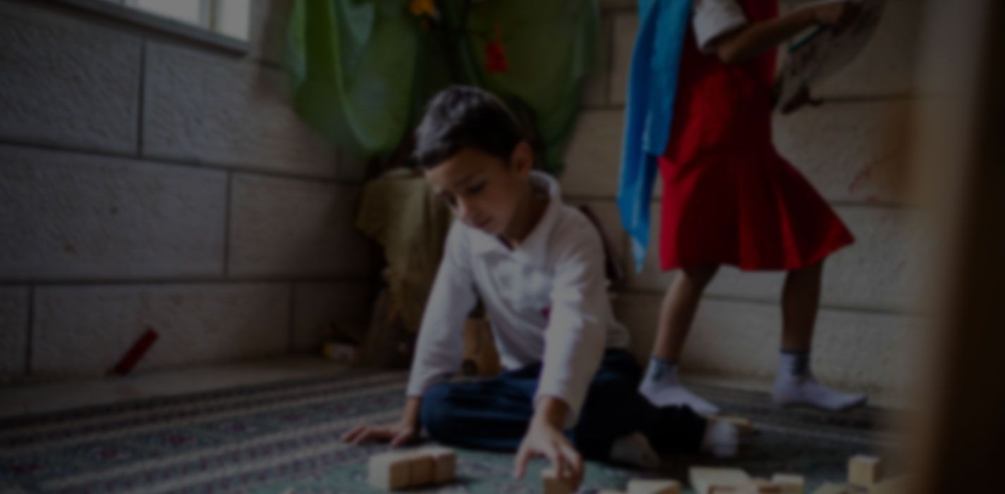 A boy and a girl are playing with wooden blocks on the floor.