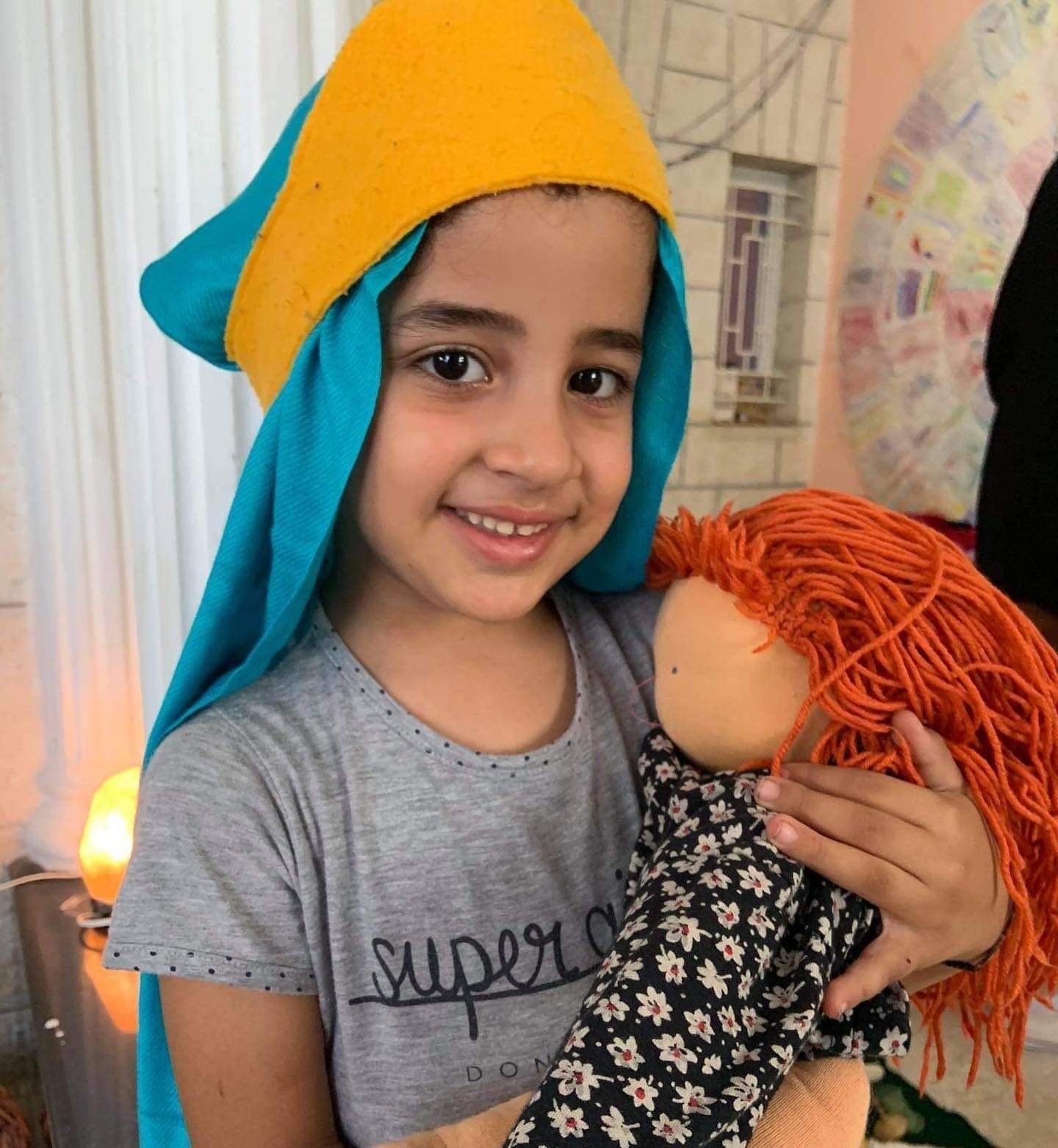 A little girl wearing a super t-shirt is holding a doll