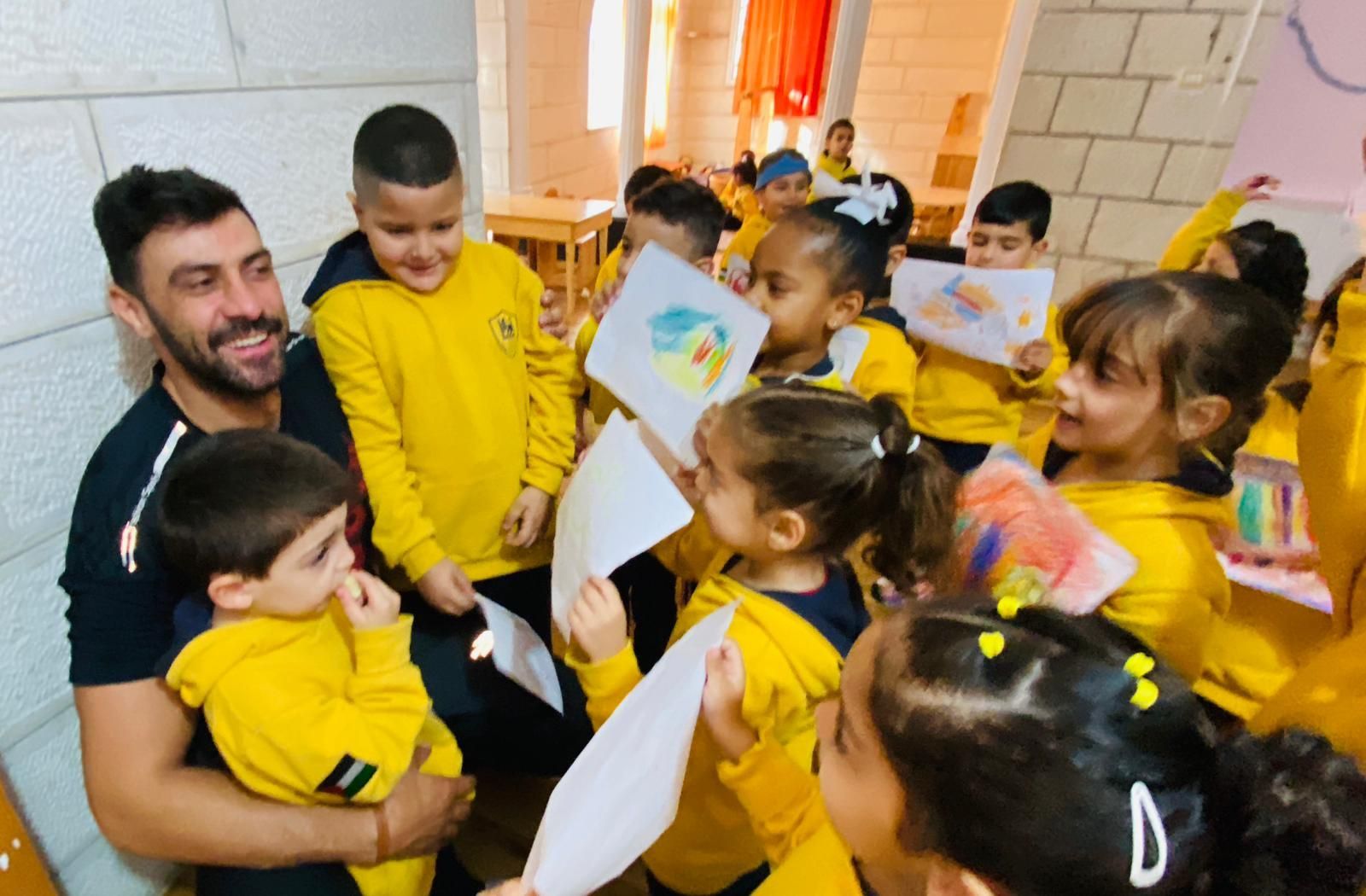 A group of children are sitting around a man holding a piece of paper.