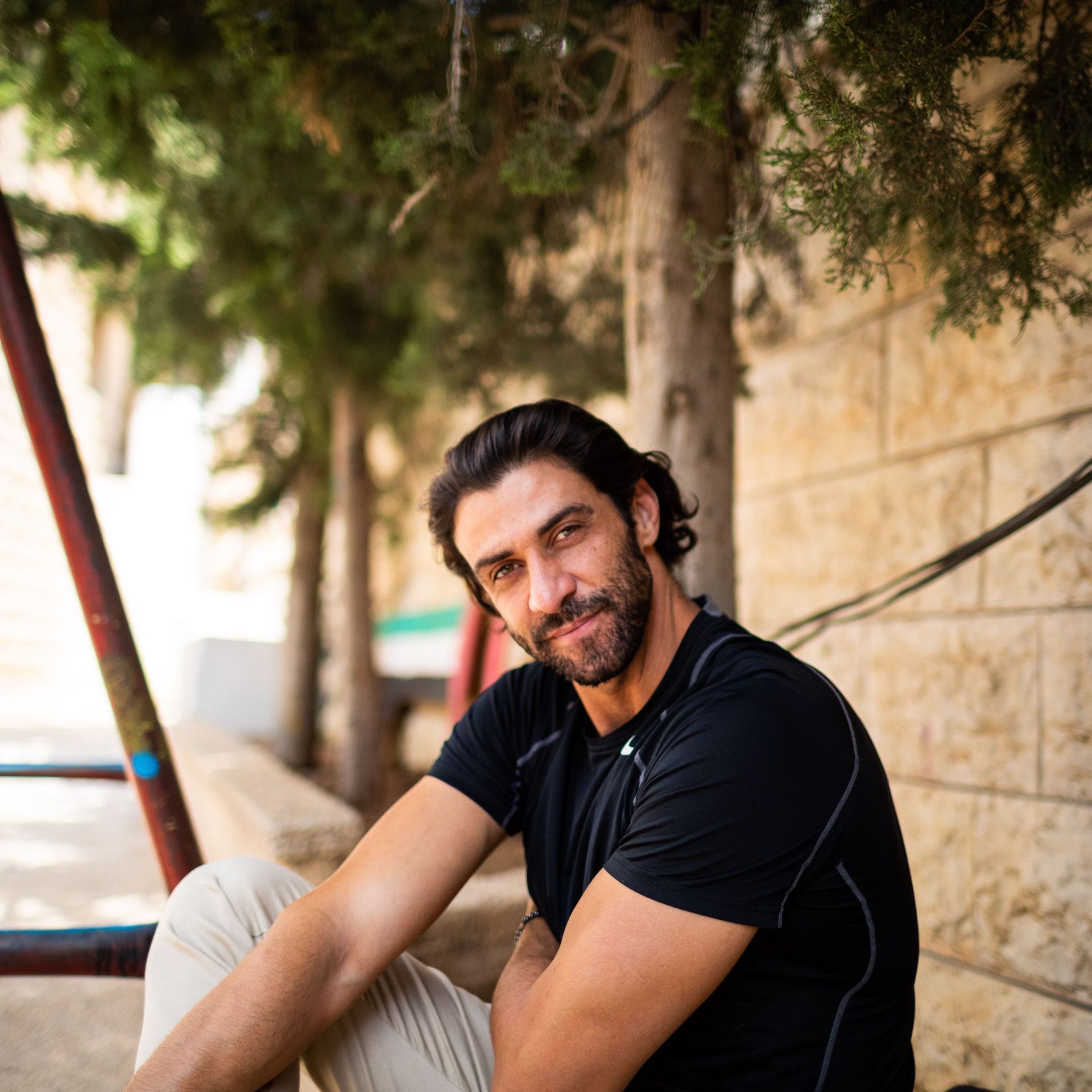 Milad Vosgueritchian, chairman of Vision Association for Culture and Arts and its House of Hope Vision School. Milad is sitting on the ground outside of a stone wall and smiling at the camera.
