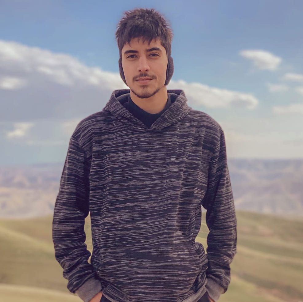 Nezar Akram, a graduate of House of Hope Vision School and potential participant for the program. Nezar is standing outdoors in front of a mountainous landscape with hands in pockets.