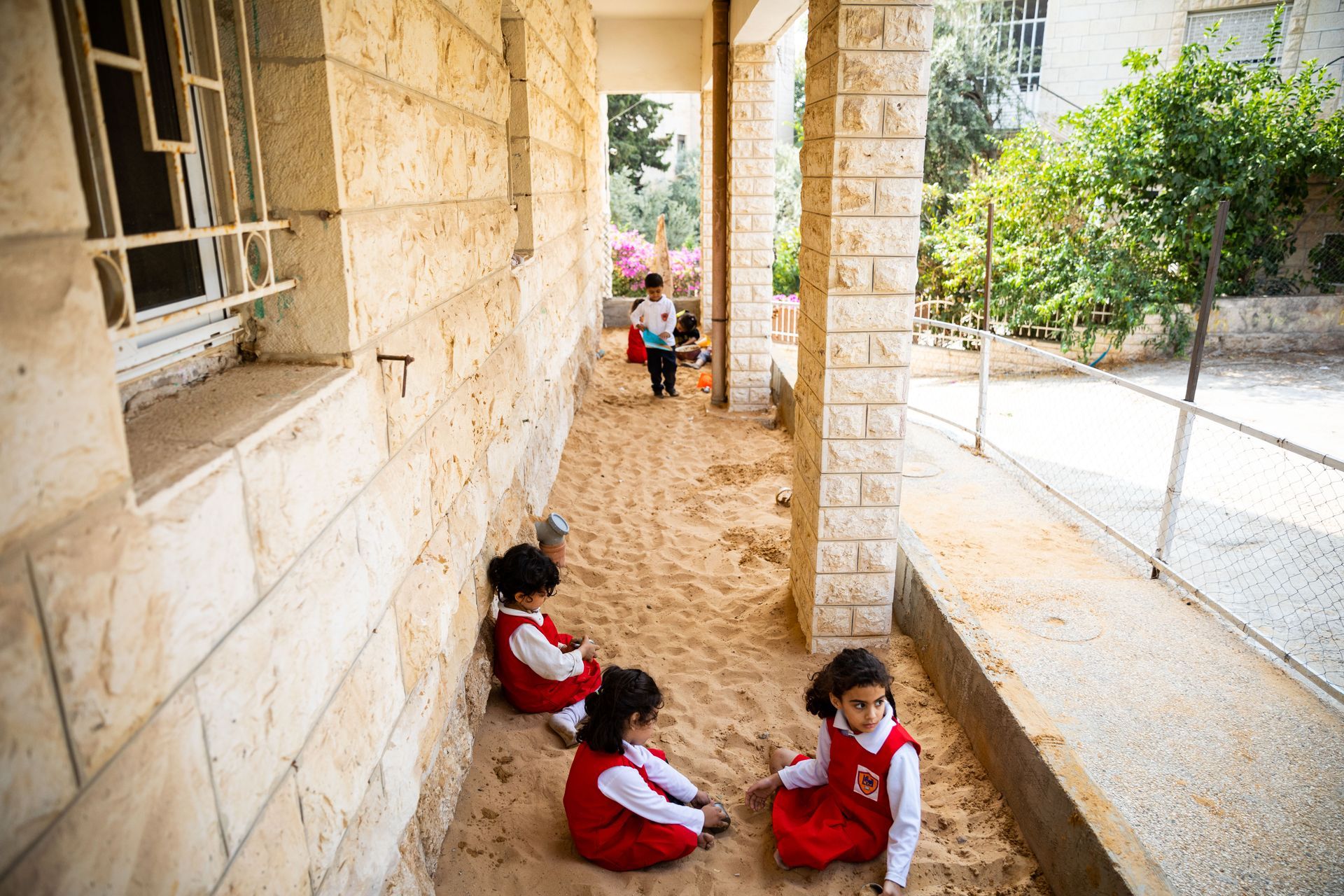 Children in red and white uniforms sitting in a stone school corridor outdoors