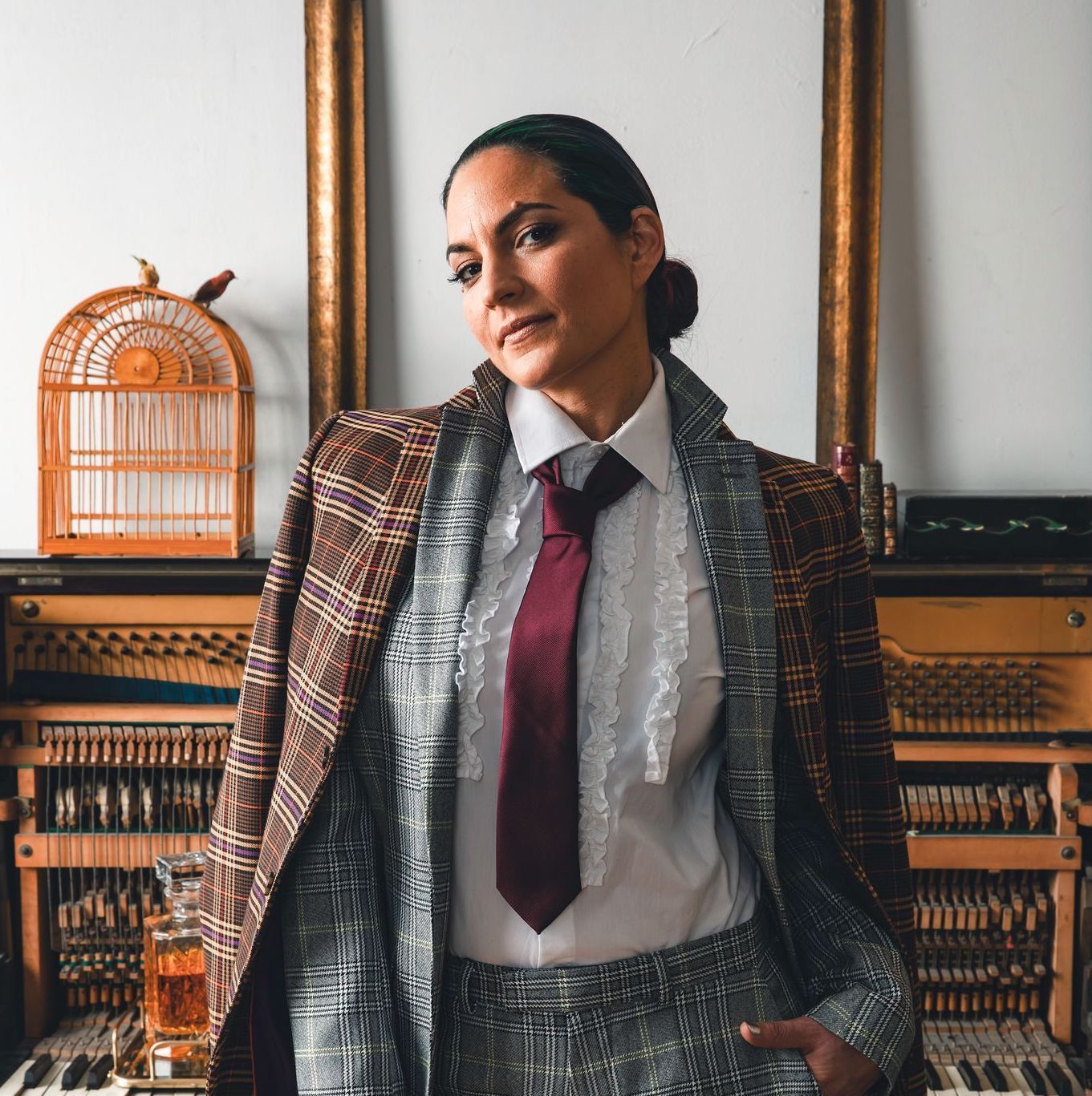 Valerie Orth, Palestine Beats Teaching Artist. Valerie is standing in front of a musical instrument, wearing a mauve tie and white collared shirt, with two plaid blazers on over it.