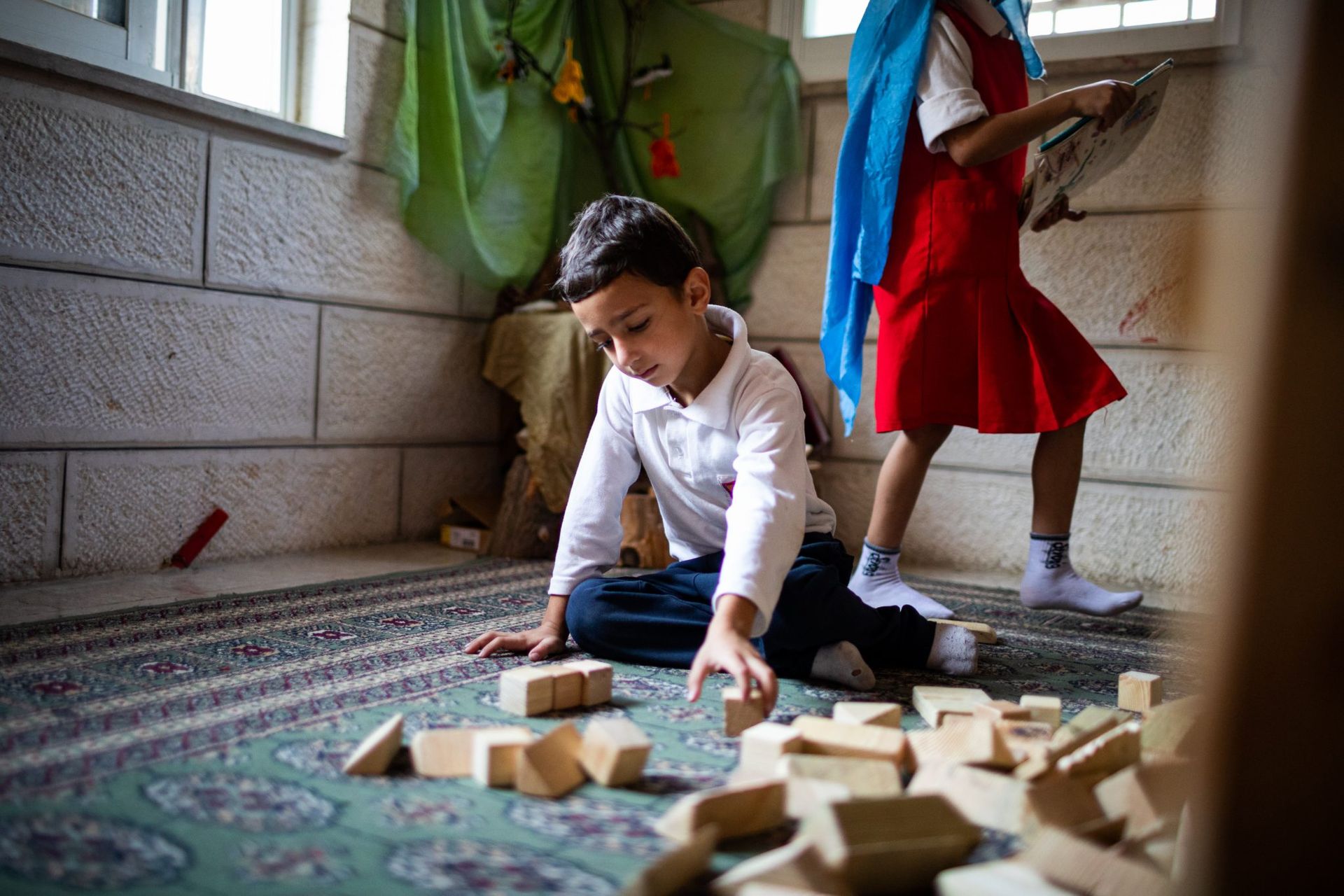 A boy and a girl are playing with wooden blocks on the floor.