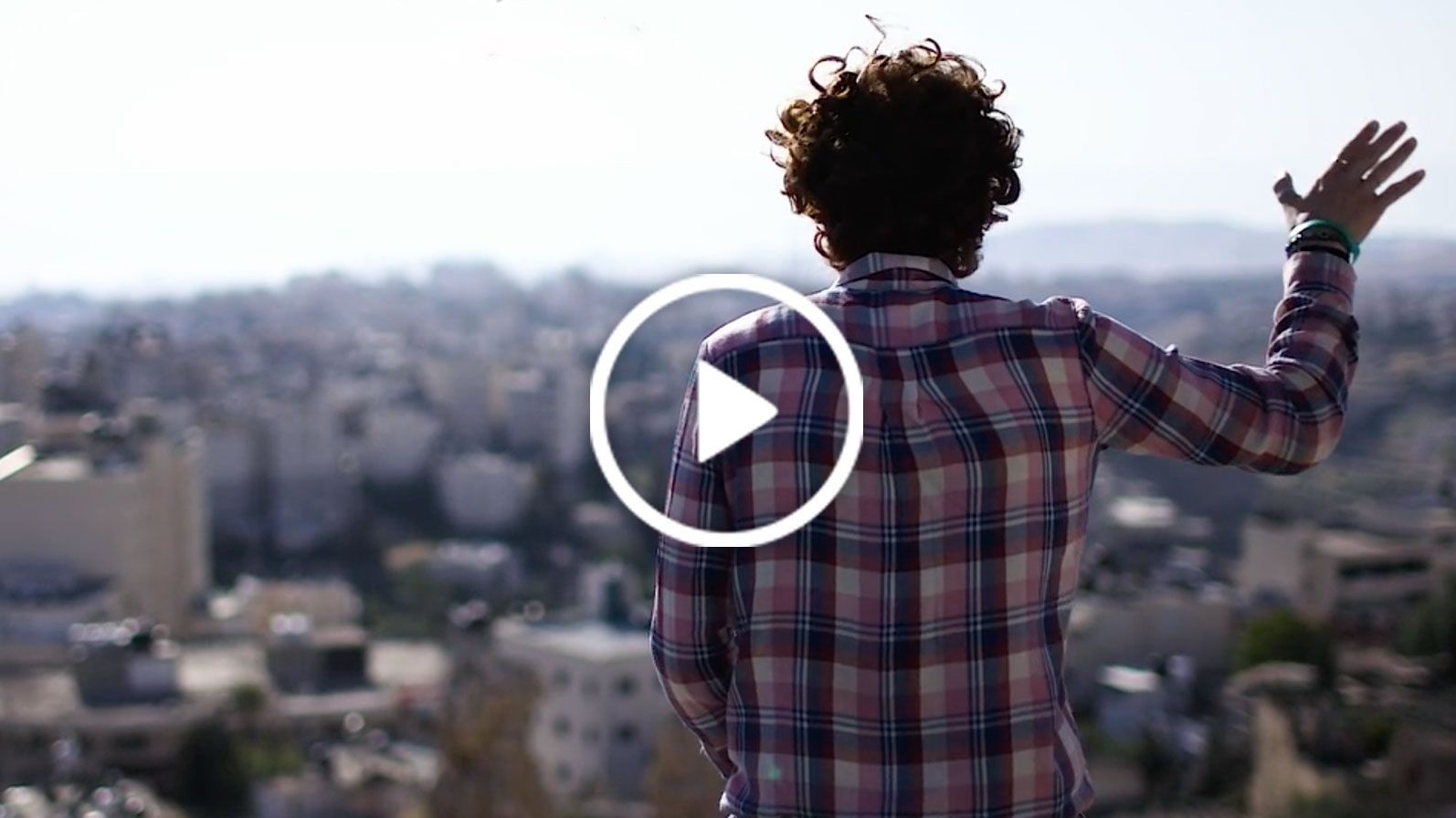 A woman in a plaid shirt is waving her hand in front of a city.