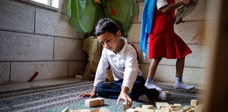 A boy and a girl are playing with wooden blocks on the floor.