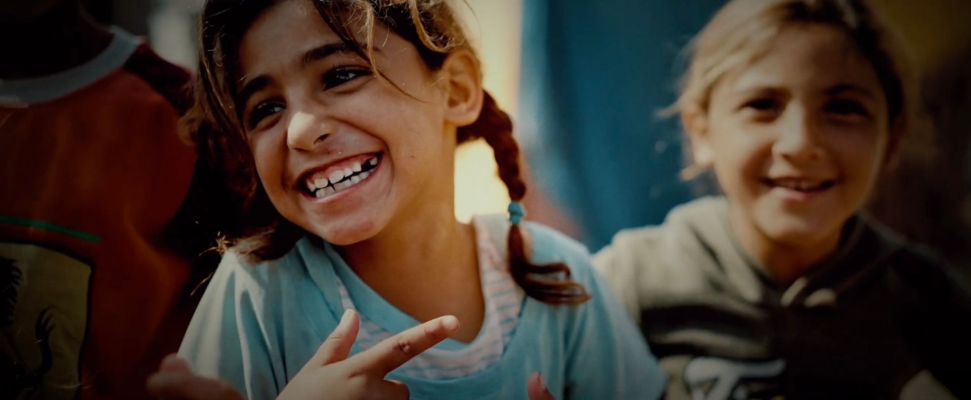 Two young Palestinian girls smiling, one pointing.