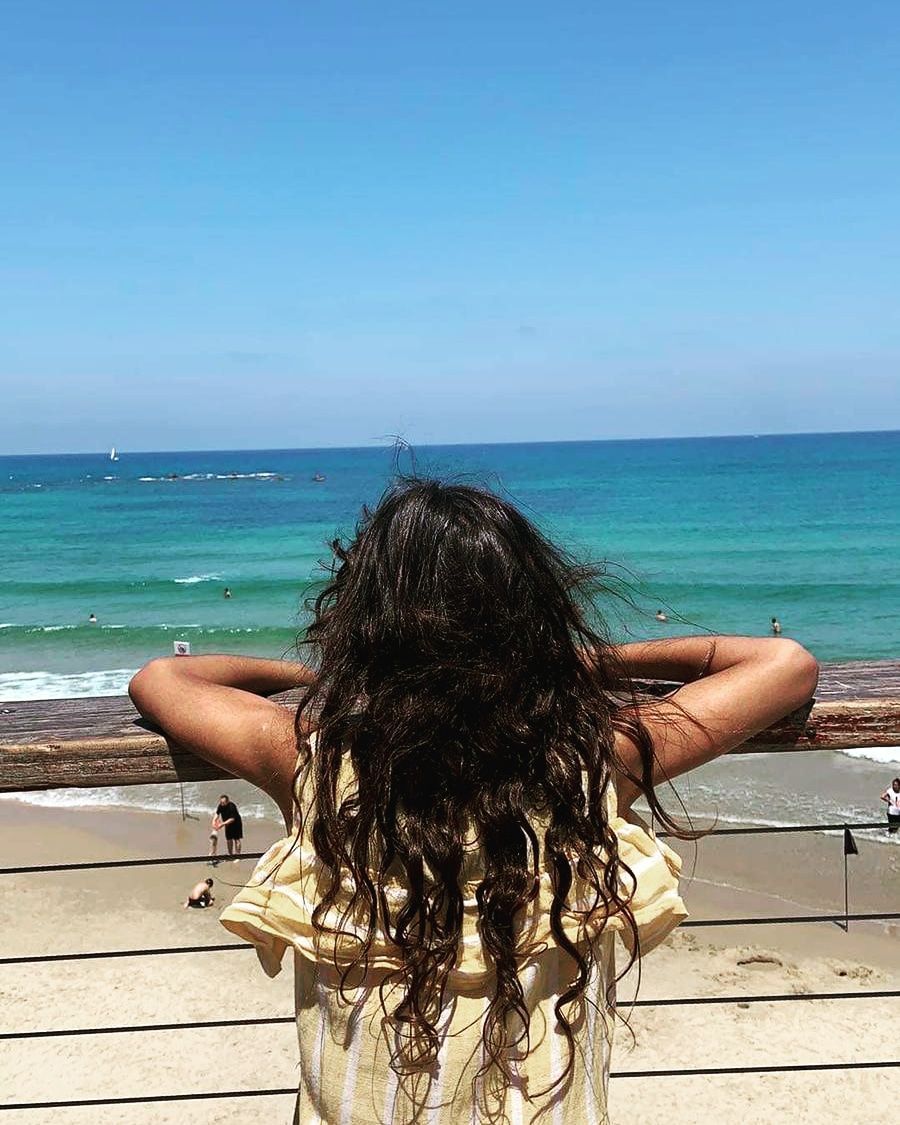A girl is standing on a beach looking at the ocean.