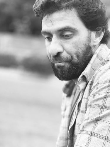 A black and white photo of a man with a beard wearing a plaid shirt.