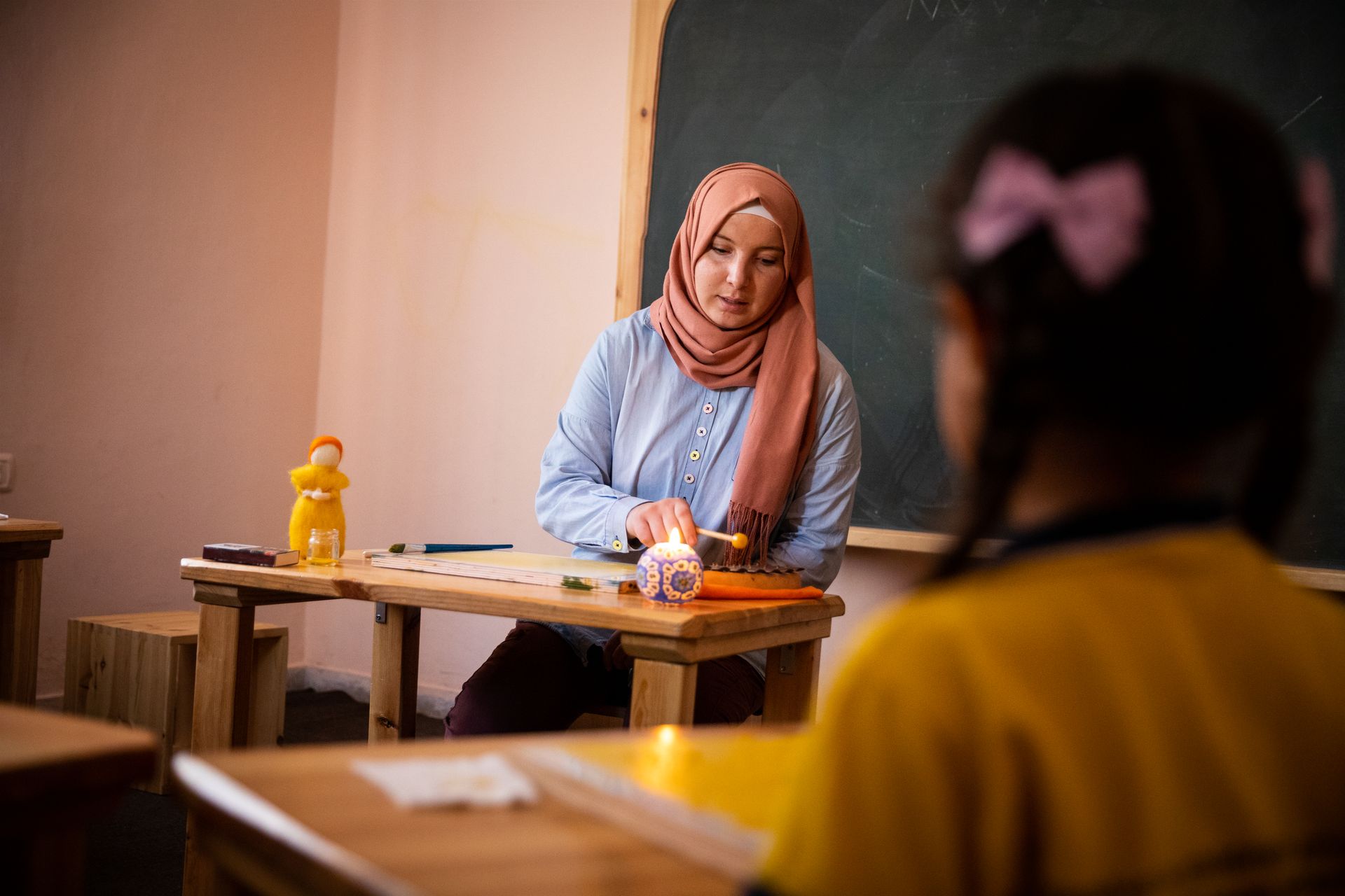 A woman in a hijab is teaching a girl in a classroom.