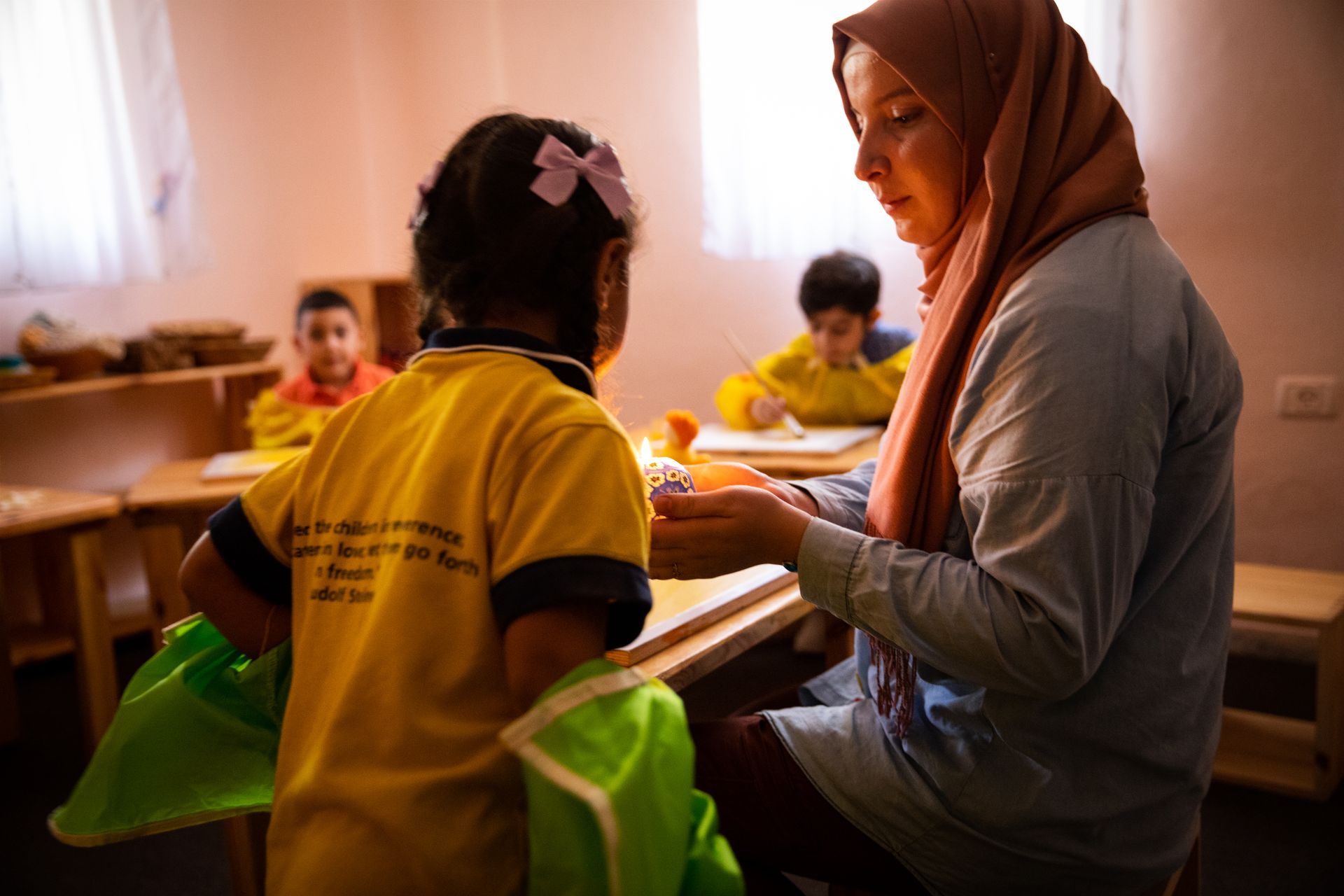 A woman in a hijab is talking to a little girl in a classroom.