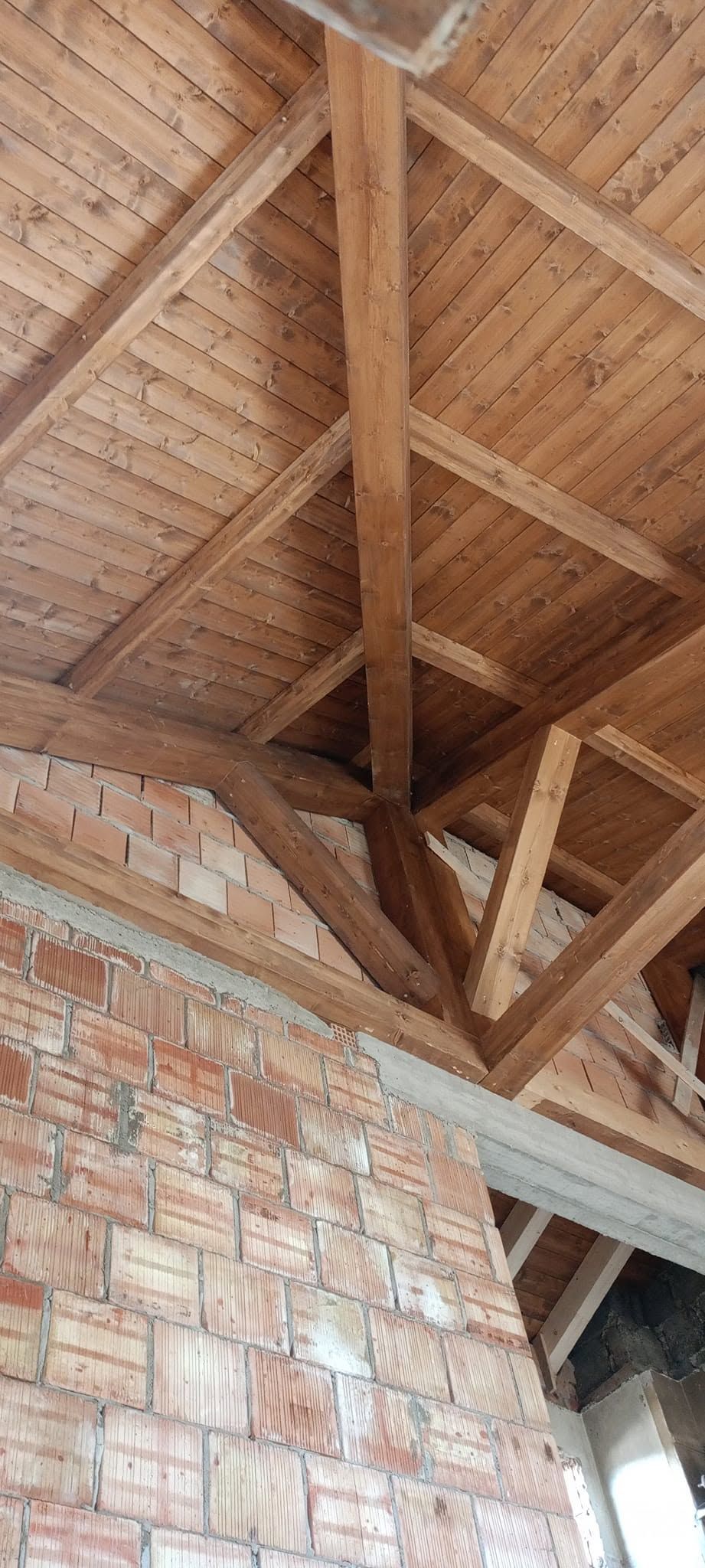 Travi in legno a vista sul soffitto, sopra un muro di mattoni e una porta all'interno di una stanza non rifinita.