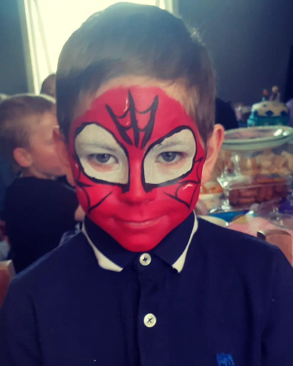 A young boy with his face painted like spider man