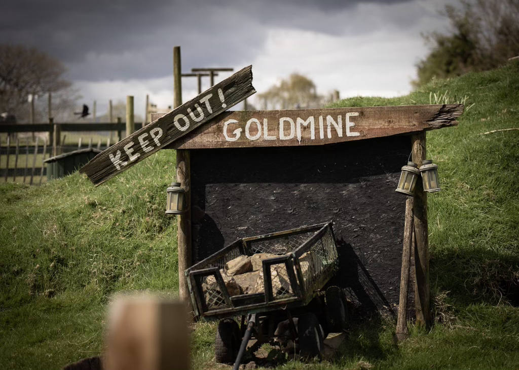 A wooden sign that says `` keep out goldmine '' is in a field.