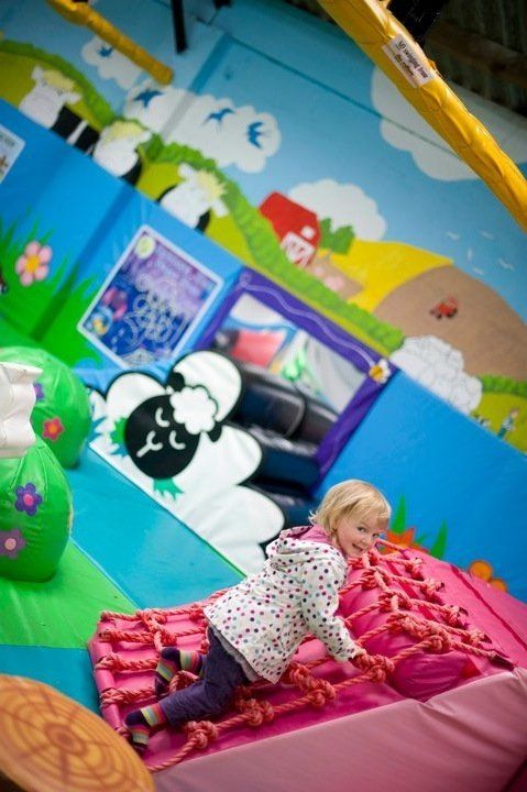 A little girl is playing in a play area with sheep on the wall.