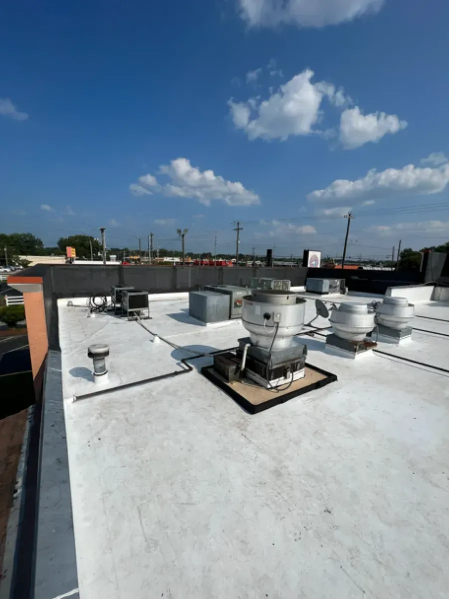 White flat roof with vents and air conditioning units under a blue sky.