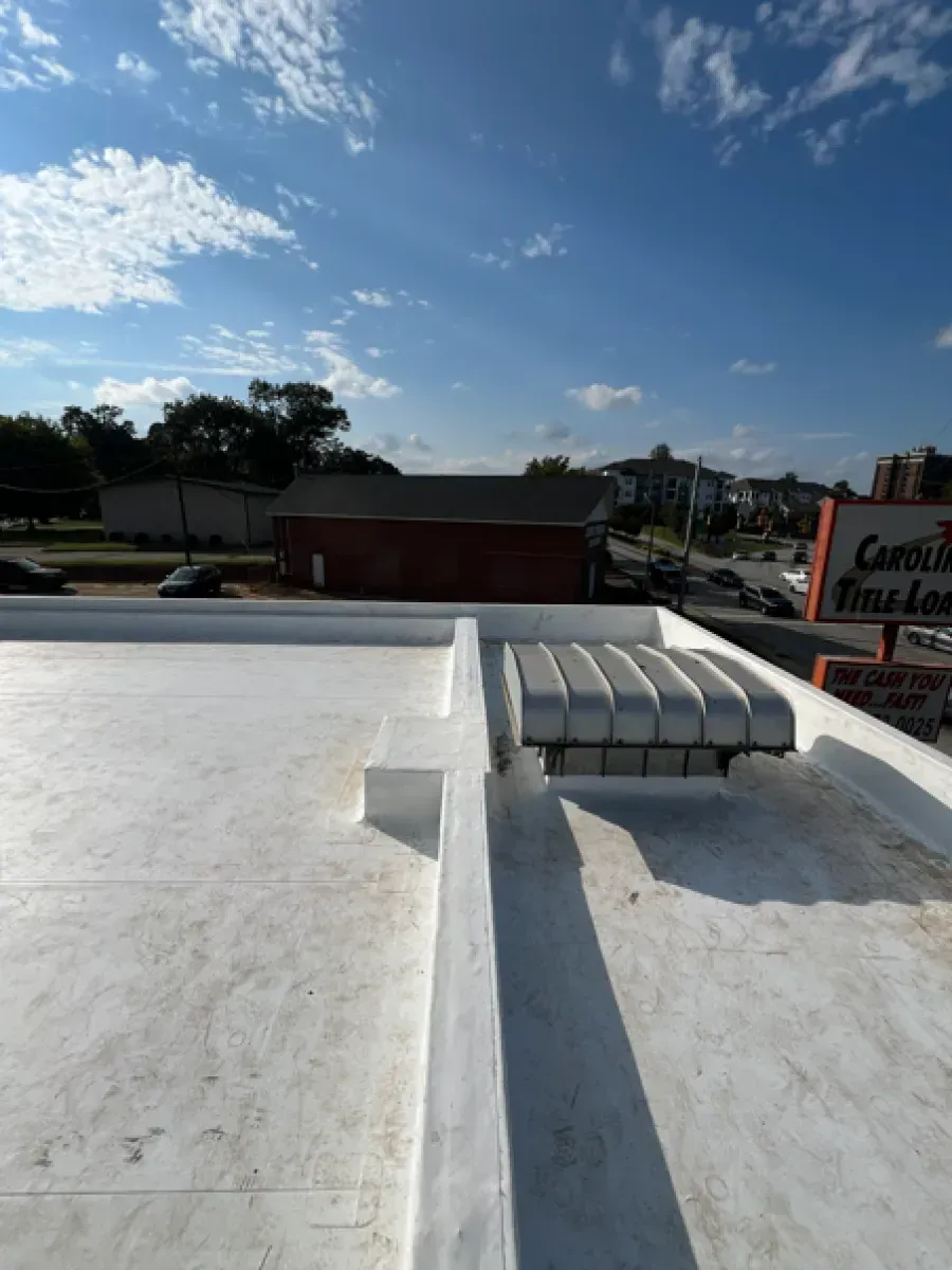 White commercial building flat roof with vents, a small brick building in the background. Bright blue sky.