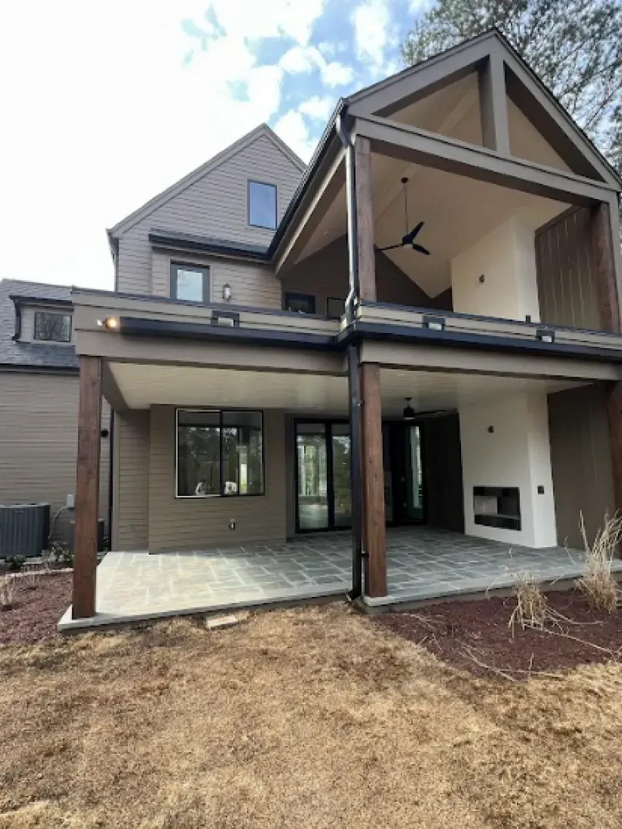 Rear exterior of a house with covered patios, a fireplace, and brown siding.