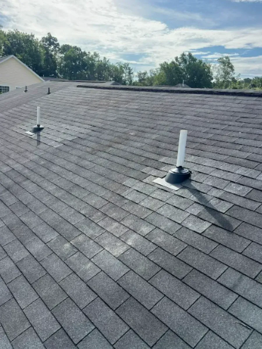 Gray asphalt shingle roof with two white vent pipes, blue sky in the background.