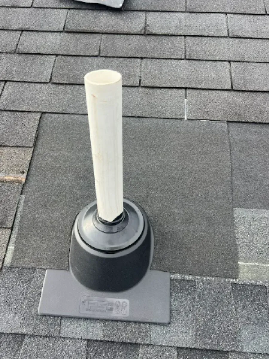 Vent pipe extending from a grey roof. The pipe is white and sits within a black rubber boot.