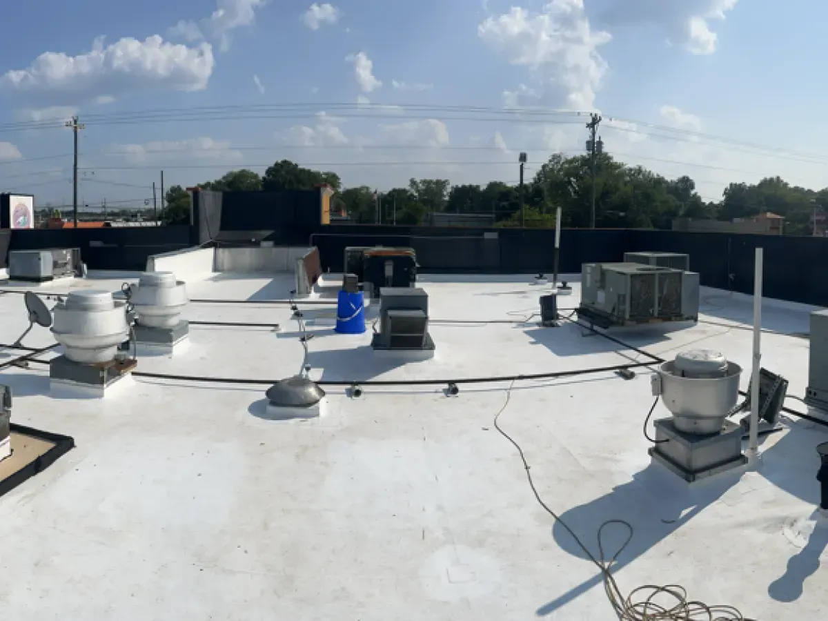 White rooftop with HVAC units, vents, and utility lines under a blue sky.