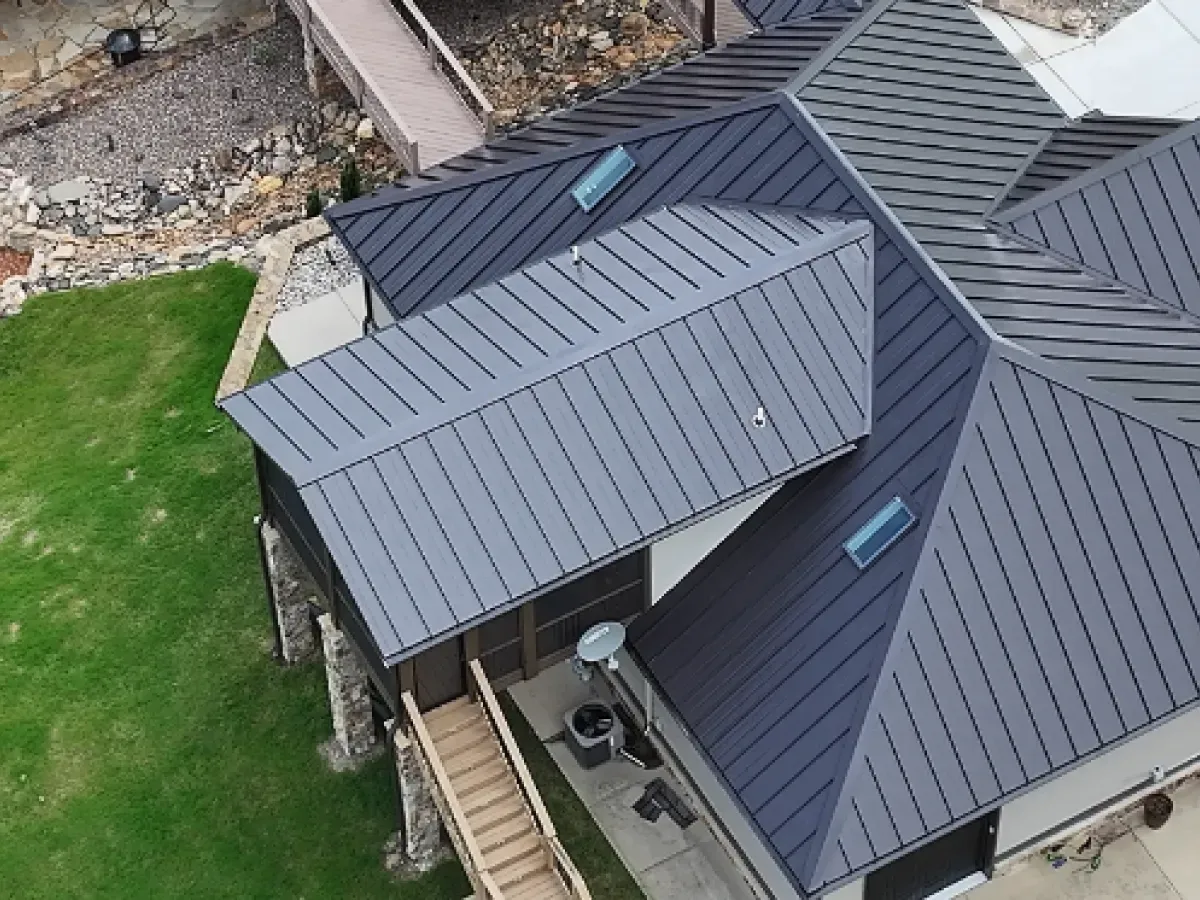 Dark gray metal roof on a house with multiple sections and skylights, viewed from above.