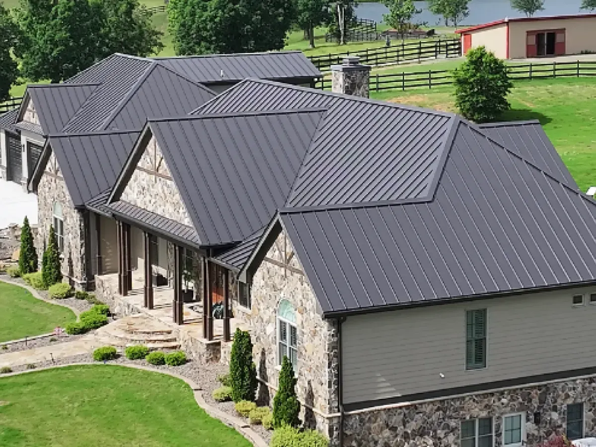 House with dark gray metal roof, stone and beige siding, and green lawn.