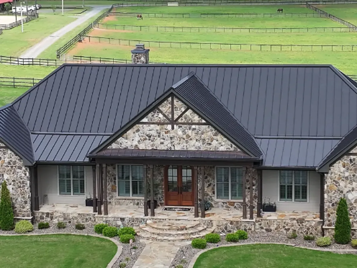 House with dark gray metal roof, stone and wood accents, set in a green field.