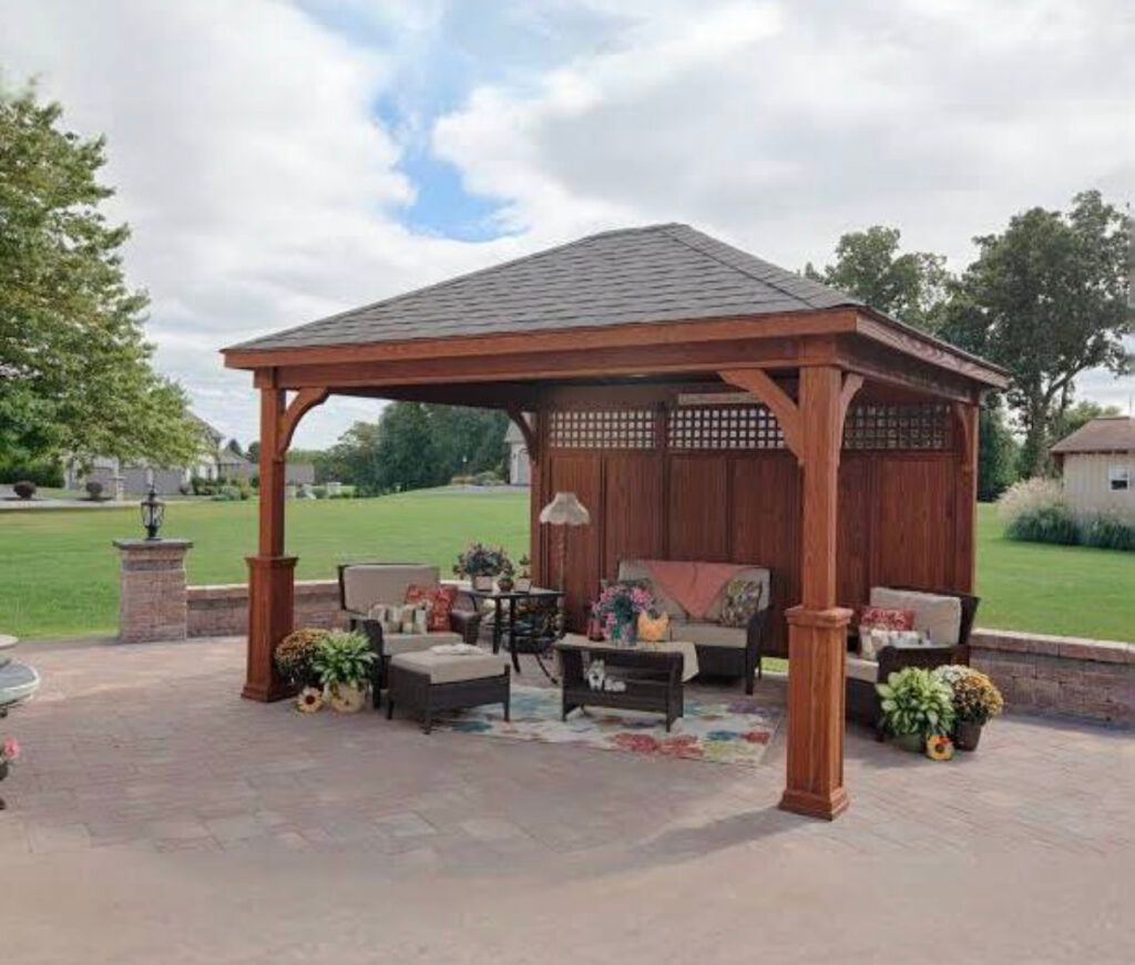 A wooden gazebo with a couch and chairs underneath it.