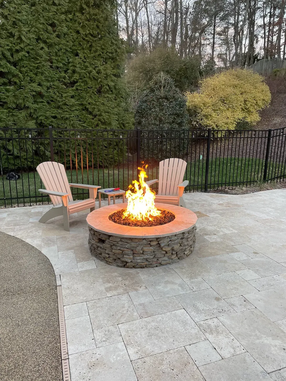 A fire pit is sitting on a patio next to two chairs.