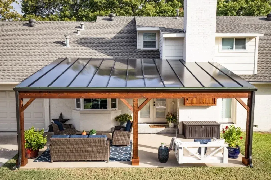 A patio with a wooden pergola and a glass roof in front of a house.
