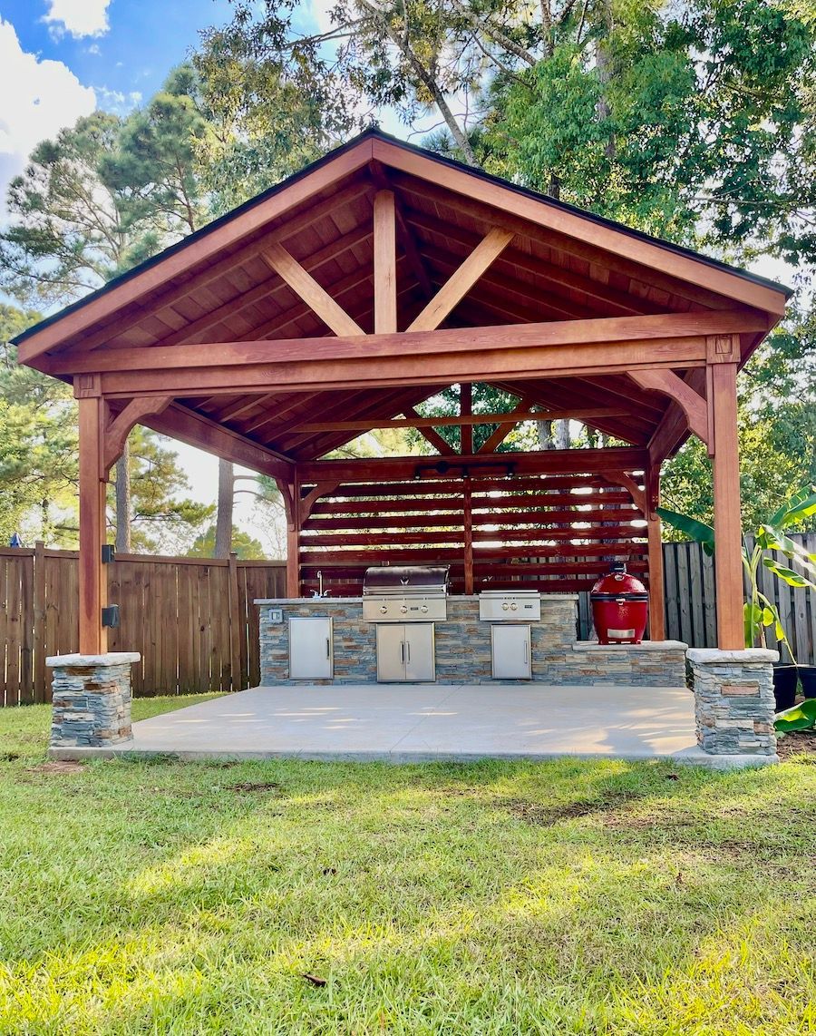 A wooden gazebo with a grill underneath it in a backyard.