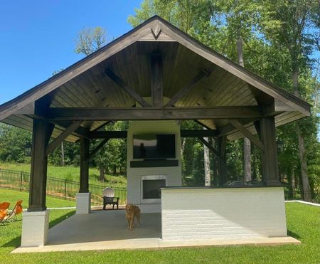 Open-air pavilion with a white counter, overlooking a grassy yard and trees, with two chairs and a dog nearby