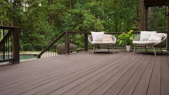 Wooden deck with two white lounge chairs overlooking a green wooded backyard
