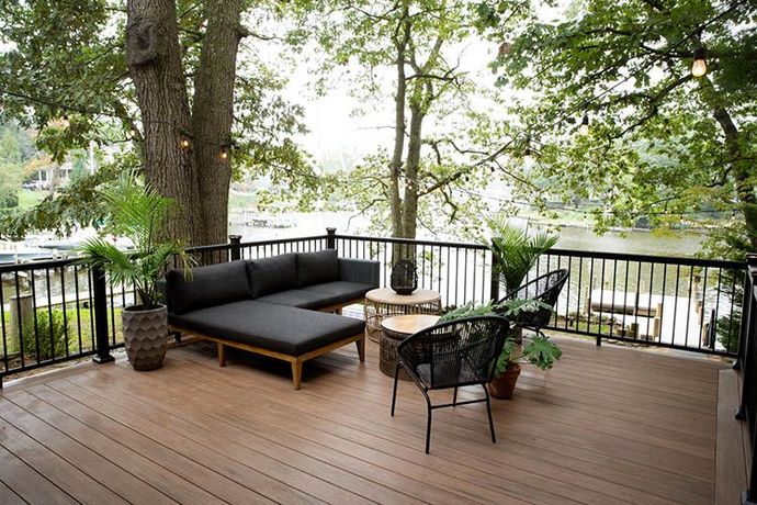 Outdoor wooden deck with black patio furniture and trees overlooking a water view