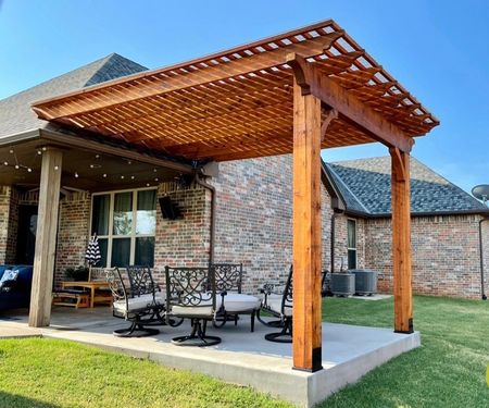 Backyard patio with wooden pergola, outdoor table and chairs beside a brick house