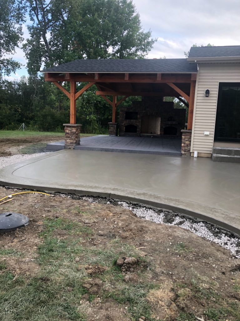 A concrete patio in front of a house with a wooden gazebo.