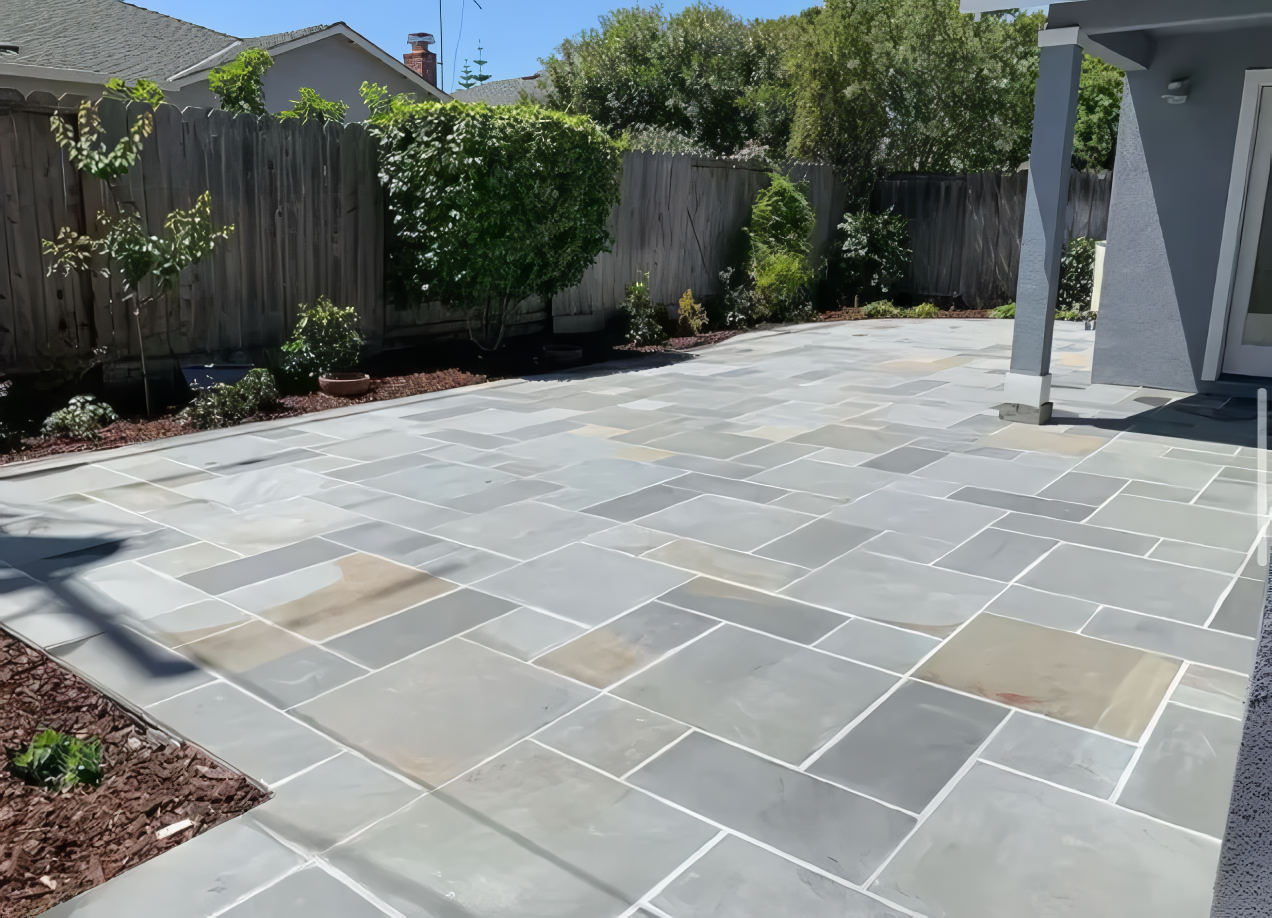 A patio with a fence in the background and a house in the background.