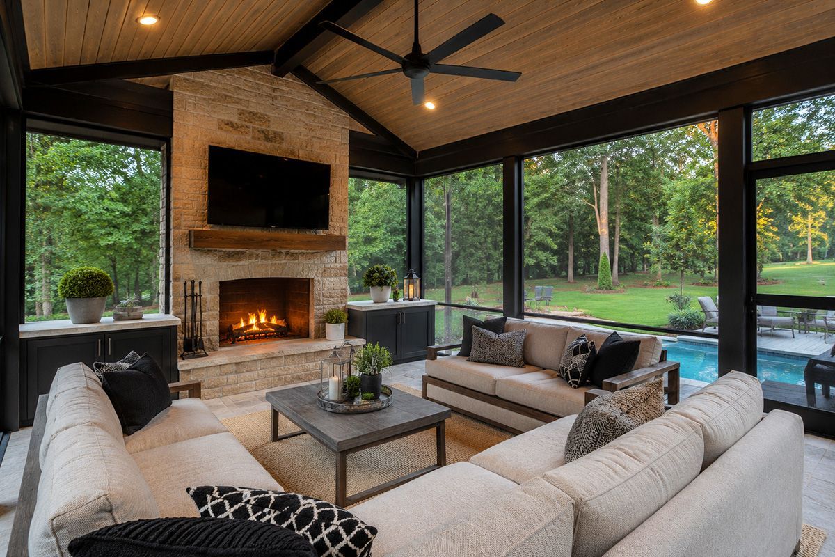 Modern covered patio with sectional seating, fireplace, TV, and pool views through glass walls